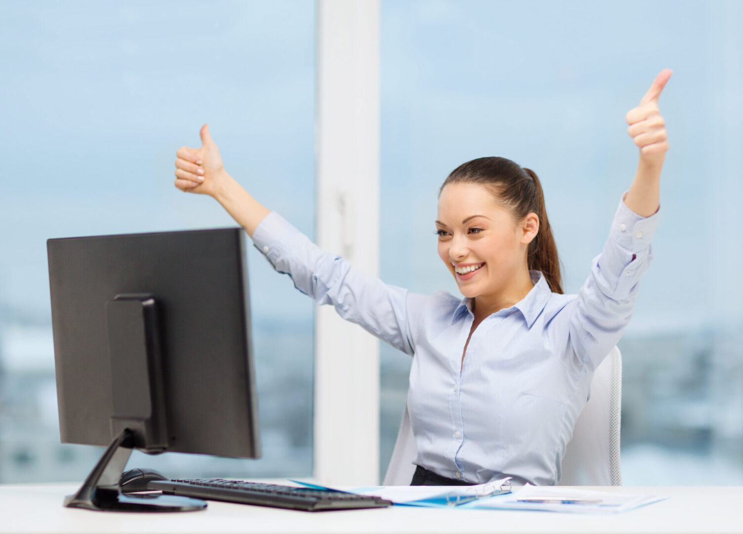 A business woman sitting at her computer celebrating a success.