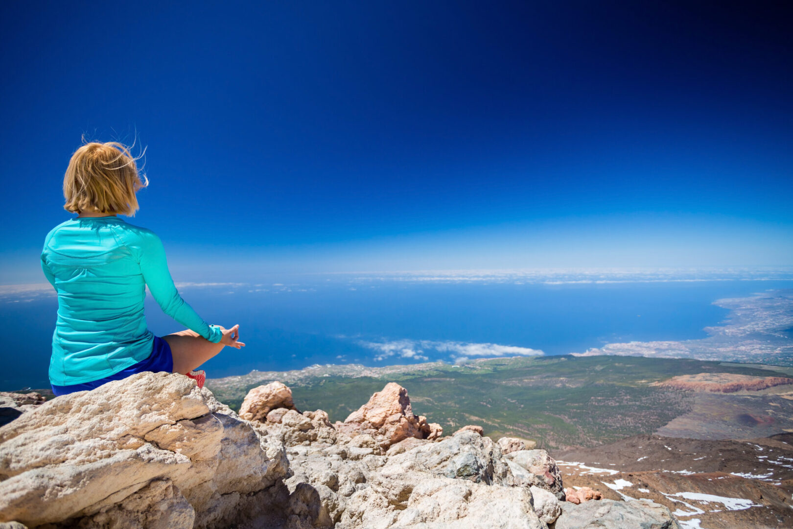 Young woman doing yoga meditation outside natural beautiful inspirational environment fitness and exercising motivation and inspiration in sunny mountains over blue sky and ocean sea.