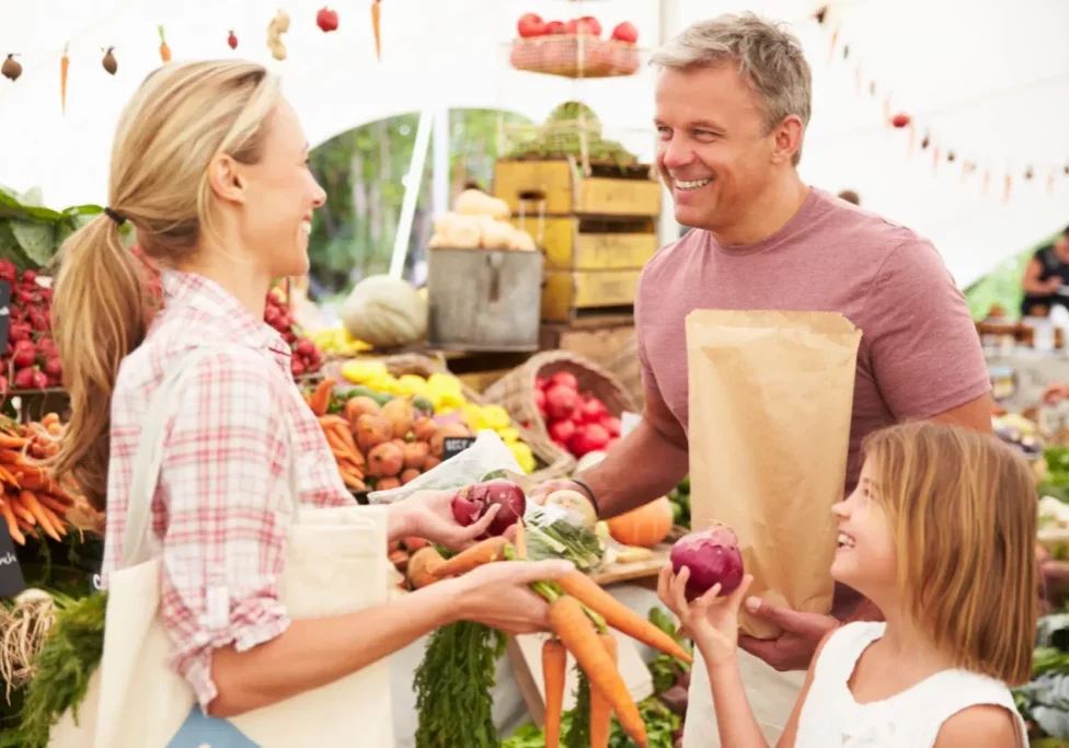 Family Buying Fresh Vegetables At Farmers Market Stall