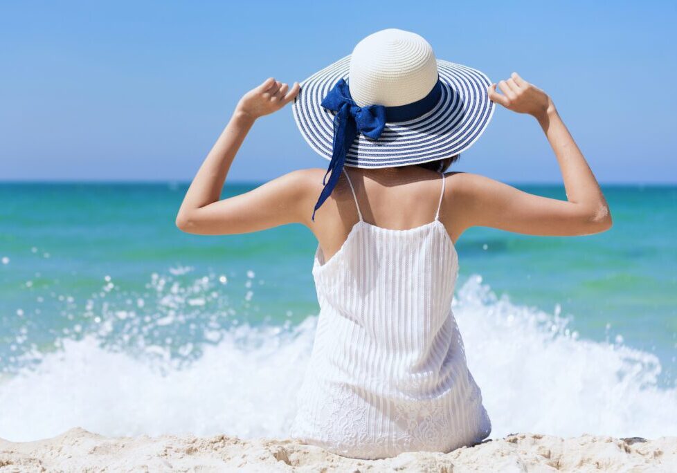 Summer time woman vacation on the beach. Cheerful woman wear summer dress and straw hats sitting on the beach look at sea.