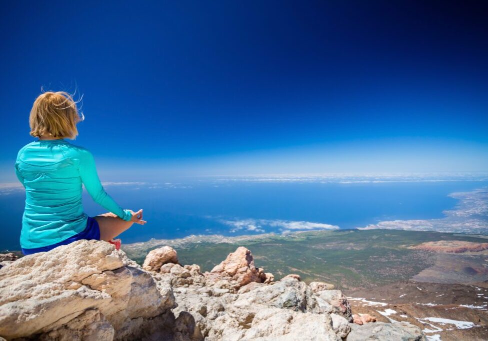 Young woman doing yoga meditation outside natural beautiful inspirational environment fitness and exercising motivation and inspiration in sunny mountains over blue sky and ocean sea.