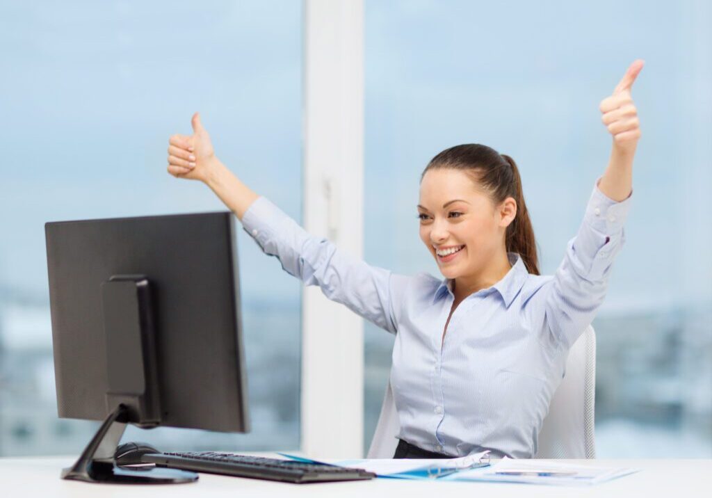 A business woman sitting at her computer celebrating a success.